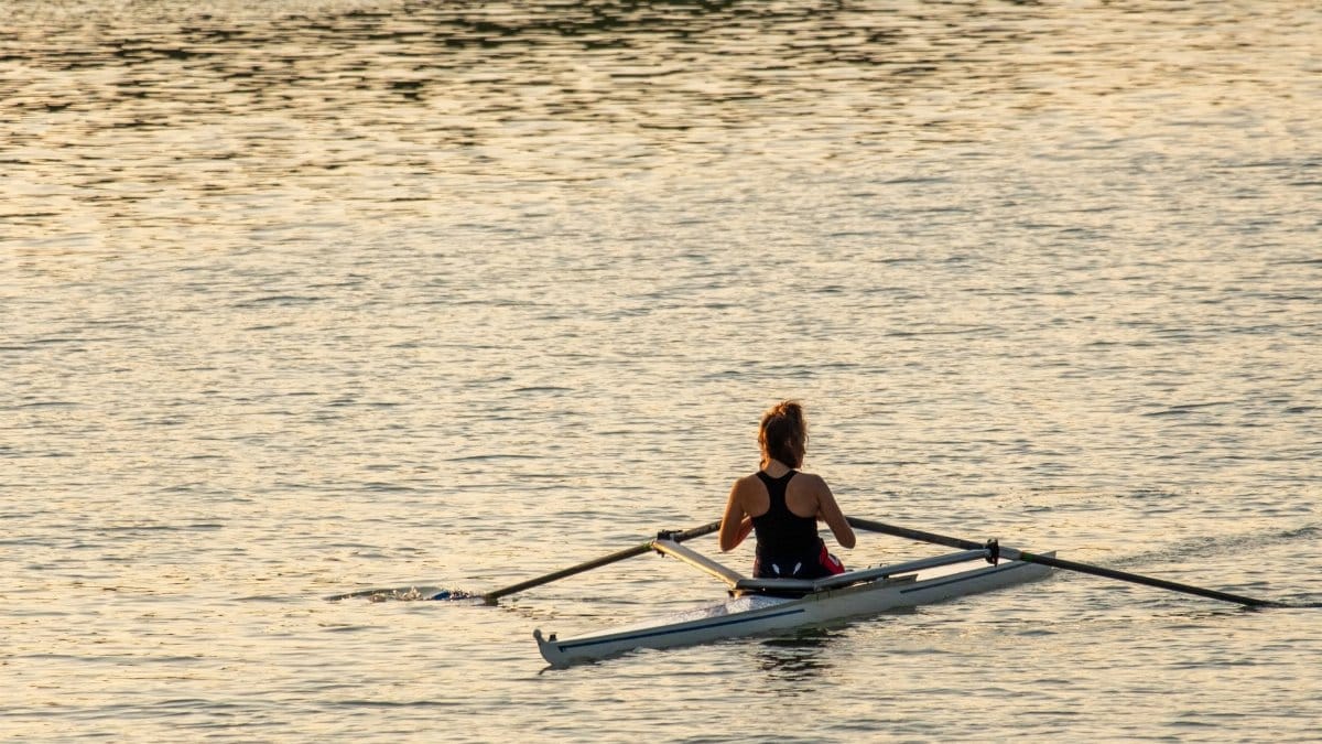 A woman rowing a boat on calm waters during a beautiful sunset.