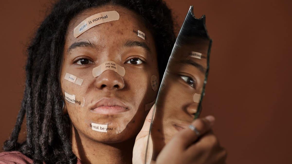 A powerful portrait of a woman embracing imperfections with positive messages on her face, holding a broken mirror.