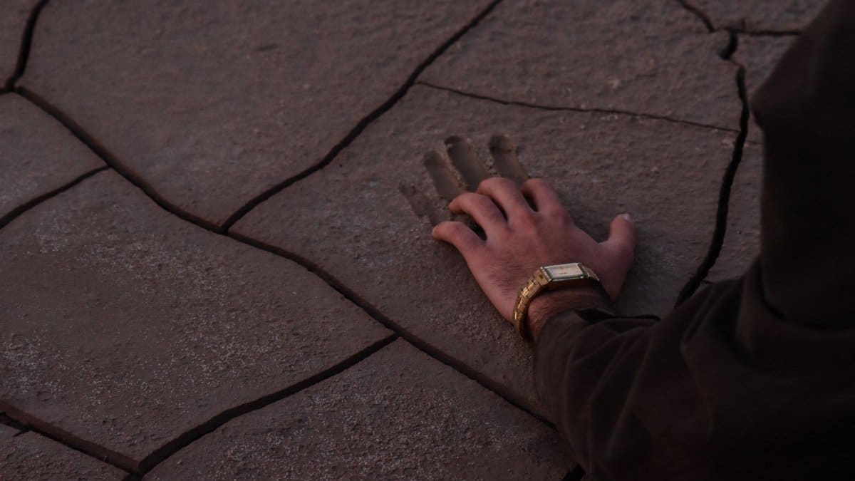 Close-up of a hand pressing into cracked desert ground, symbolizing connection with nature.