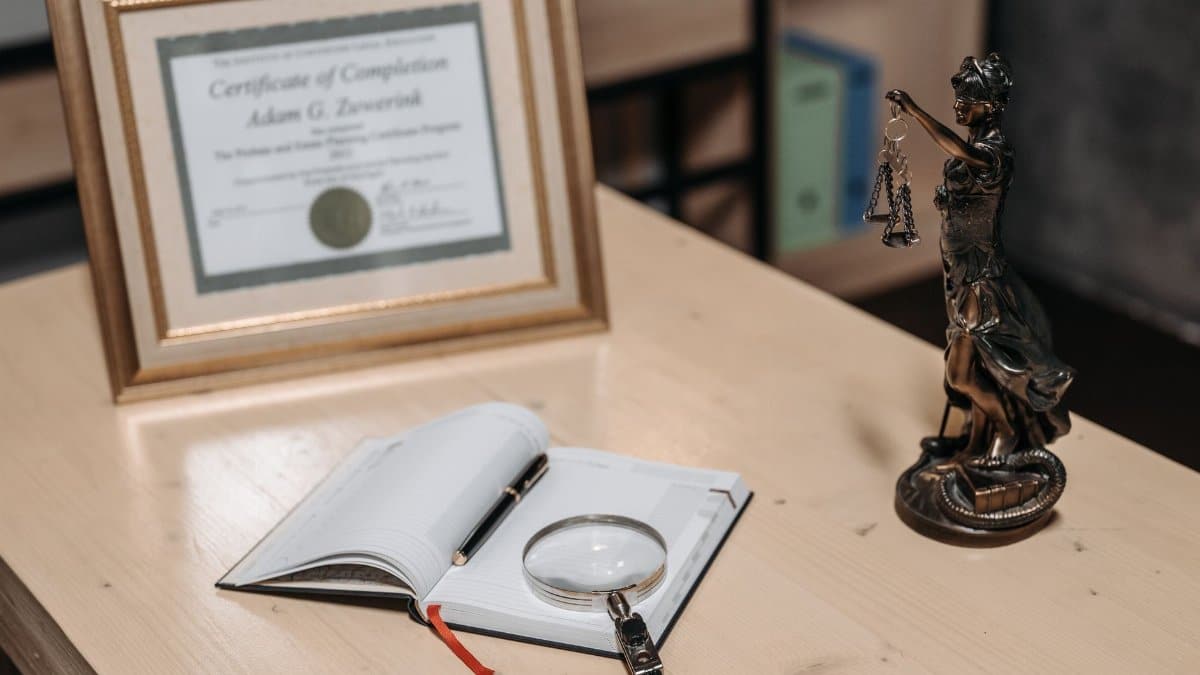 A framed certificate with Lady Justice statue on a wooden desk.