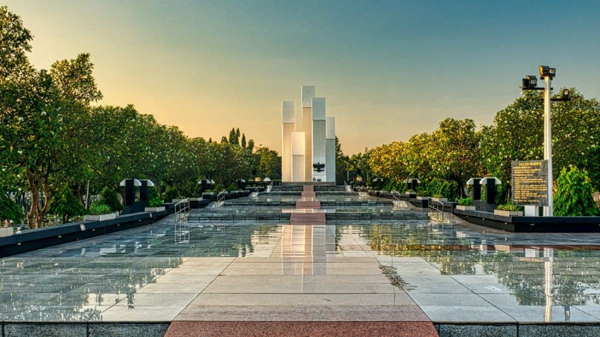 Granite pathway with steps among lush green trees leading to modern tall building in national main heroes cemetery in Kalibata