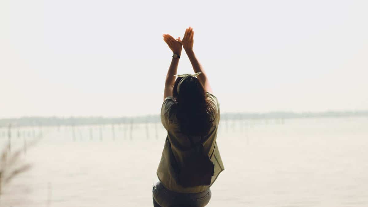 A serene moment of a woman raising her arms by a calm lake, embracing nature's tranquility.