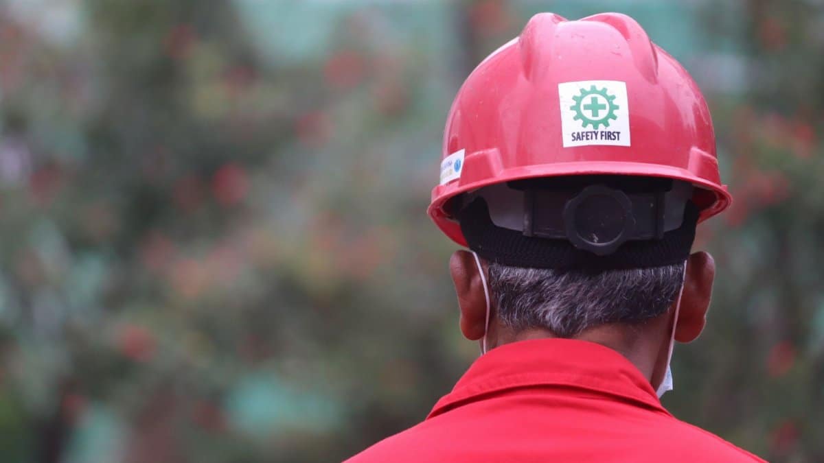 A worker focusing on safety outdoors, wearing a red helmet with a safety logo.