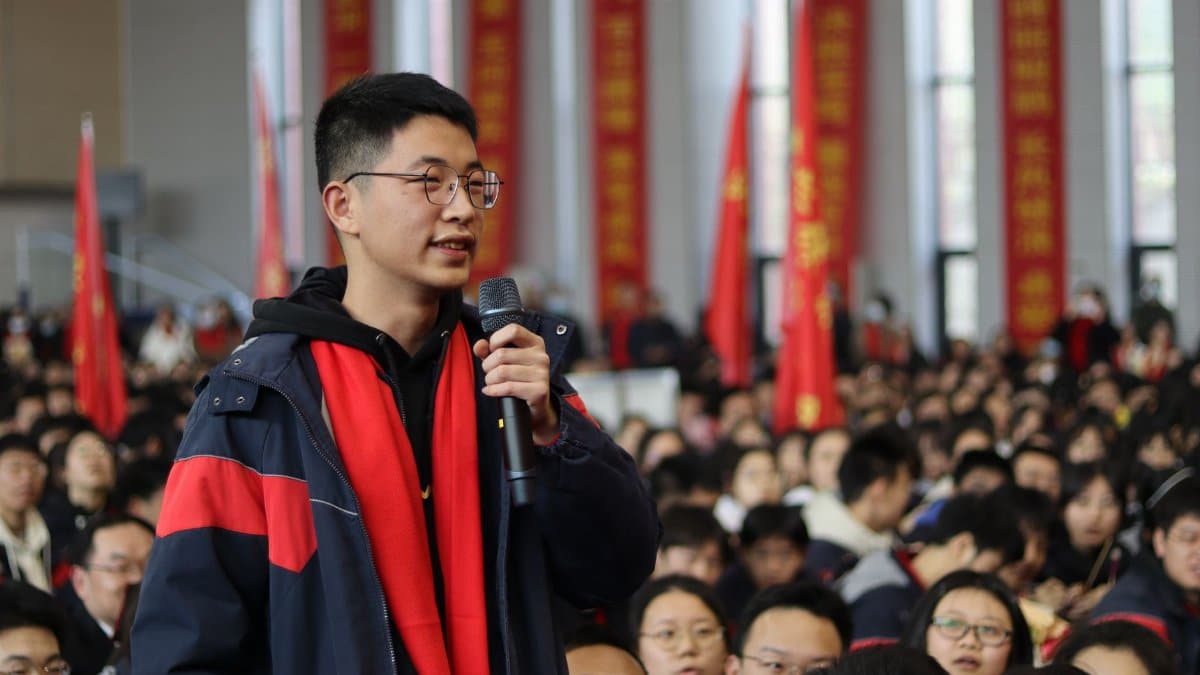 A young man speaking at a crowded indoor event, symbolizing public engagement.