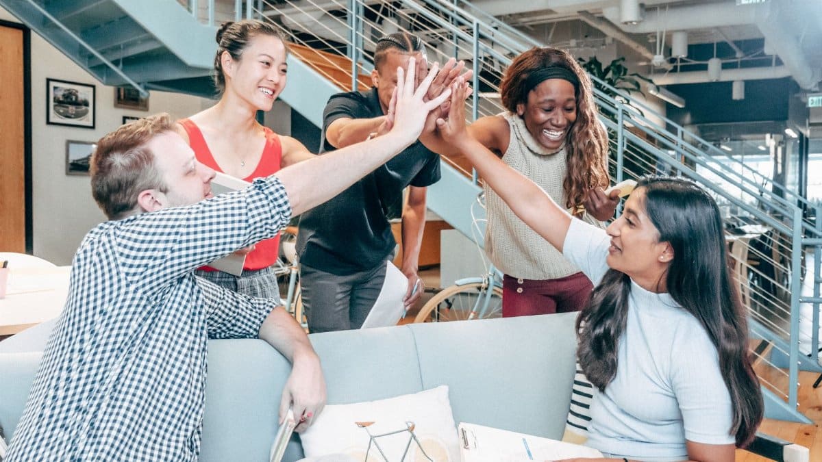 A diverse team celebrates success with a high-five in a modern office setting.