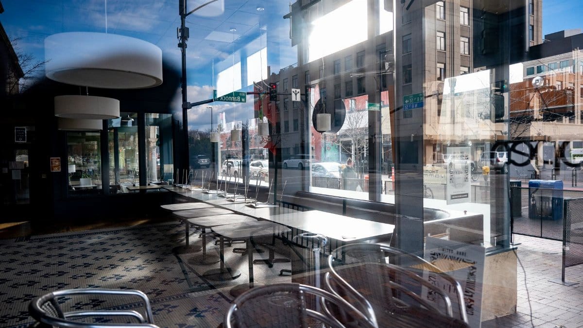 Modern cafe with reflections on glass windows, showcasing empty tables and urban street view.