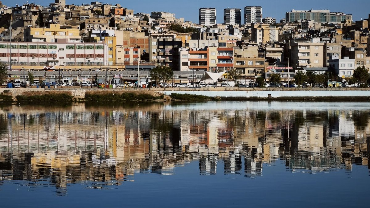 Urban cityscape with building reflections on tranquil water under a clear blue sky.