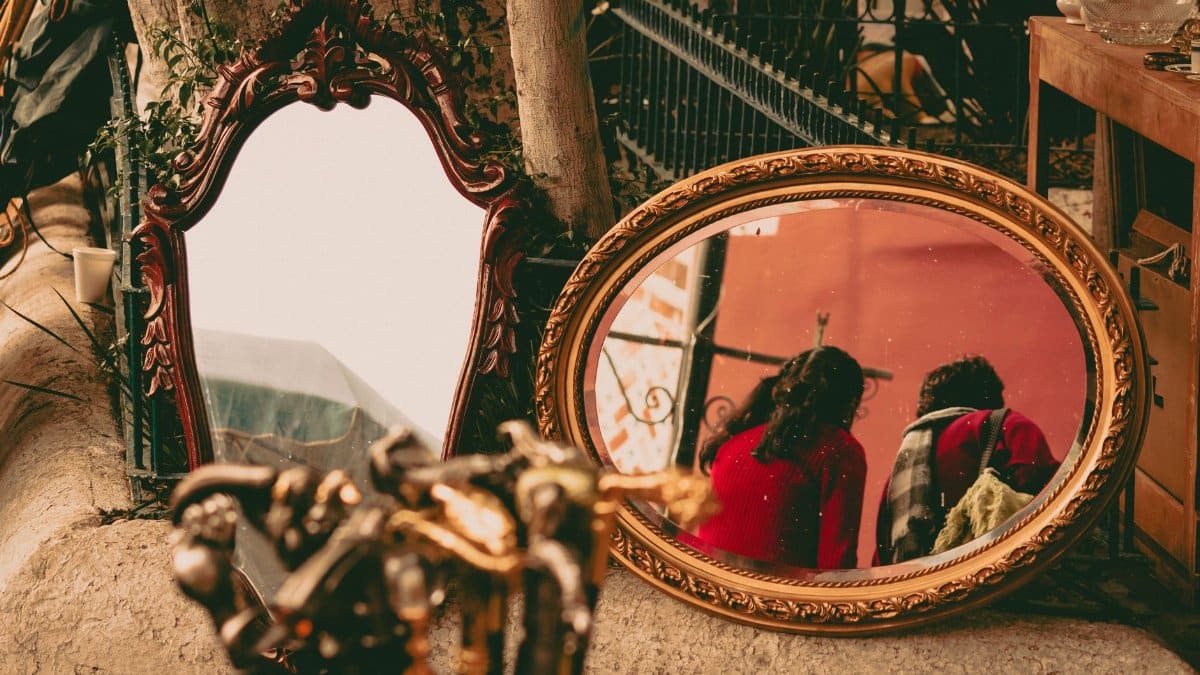 Ornate vintage mirrors at an outdoor market reflecting two women in colorful attire.