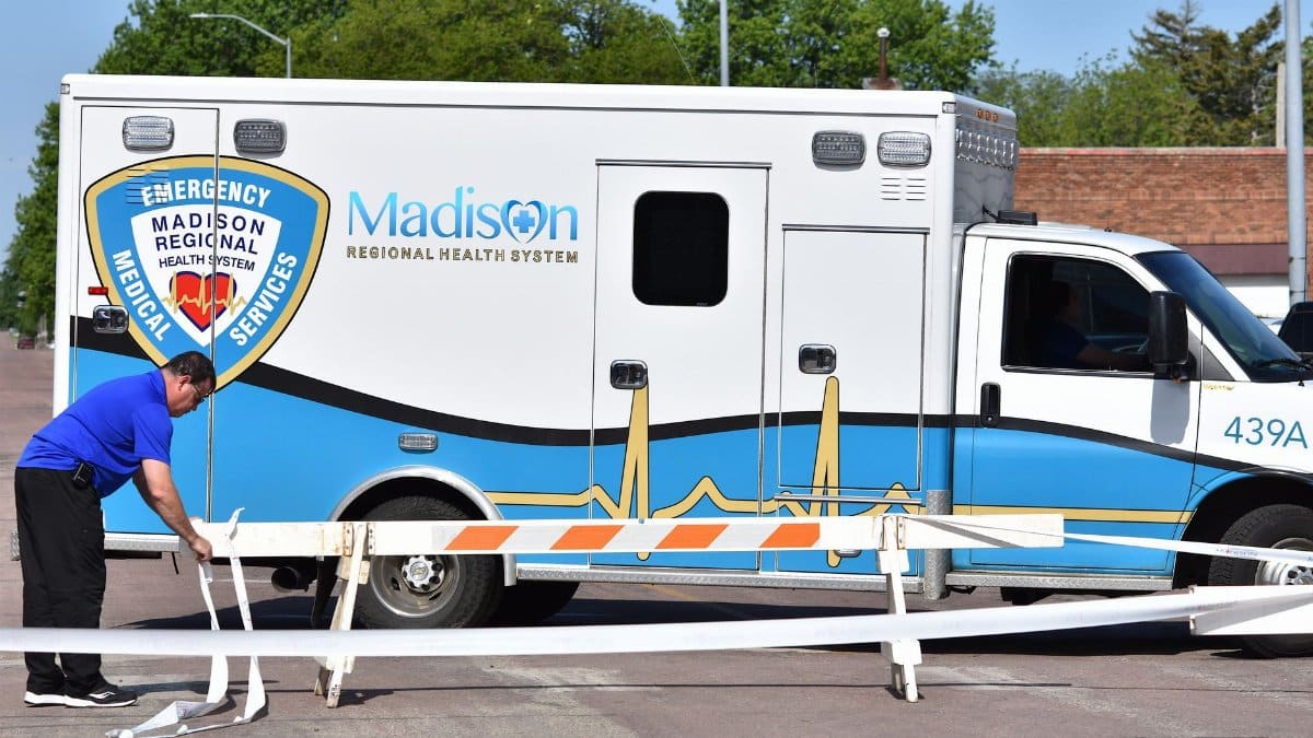 An emergency personnel adjusts barricades next to a Madison Regional Health System ambulance outdoors.