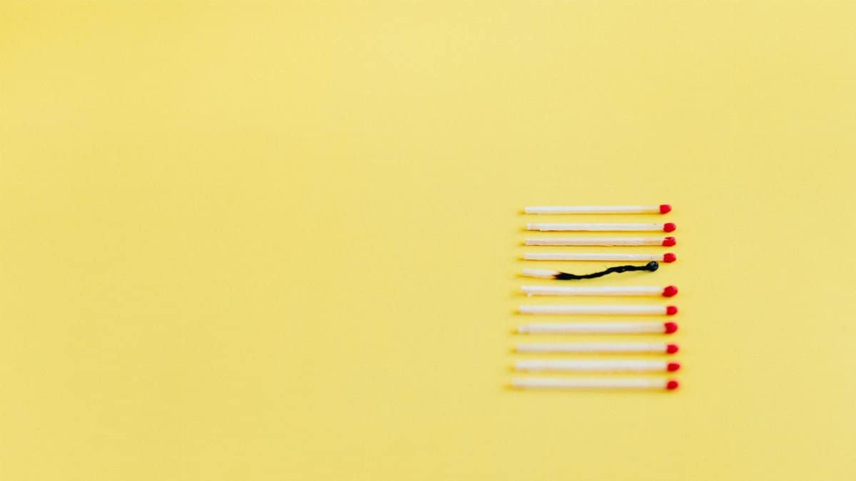 A conceptual image of burnt match among unlit ones on a yellow background, symbolizing uniqueness or burnout.