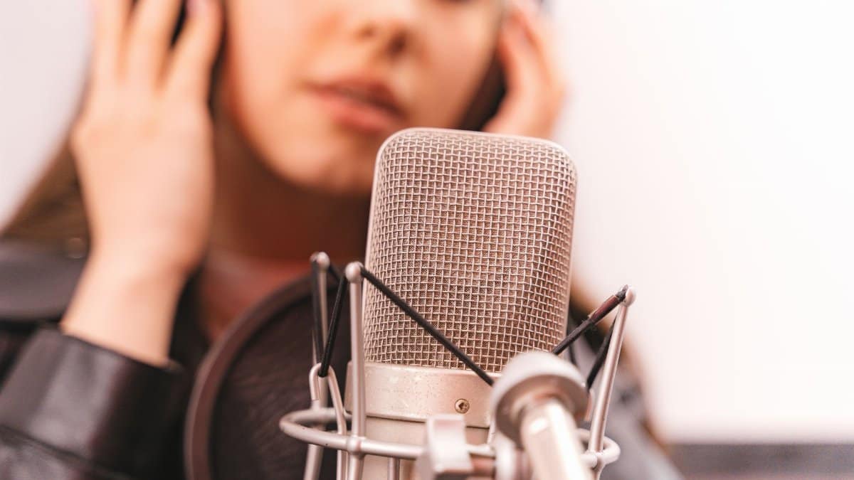 Close-up of a woman singing into a studio microphone, eyes closed, expressing emotion.