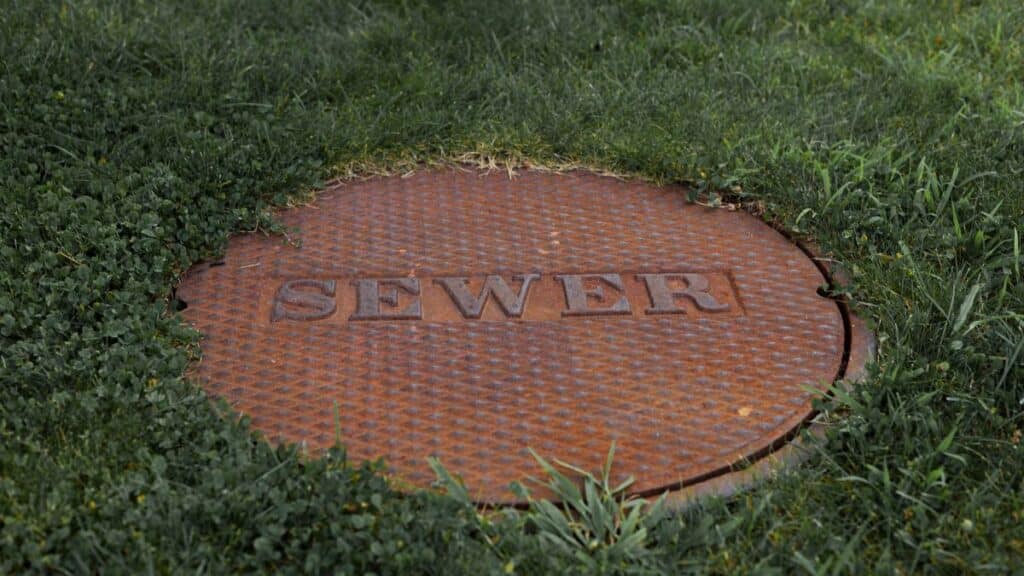 Close-up of a rusty sewer manhole cover in a grassy Boston park.