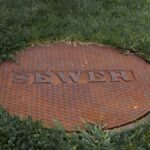 Close-up of a rusty sewer manhole cover in a grassy Boston park.