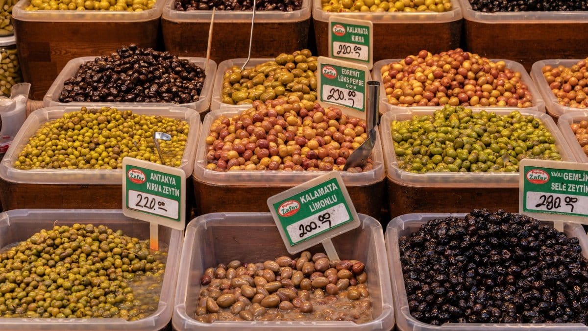 Variety of olives in containers with price tags at a market in İzmir, Türkiye.