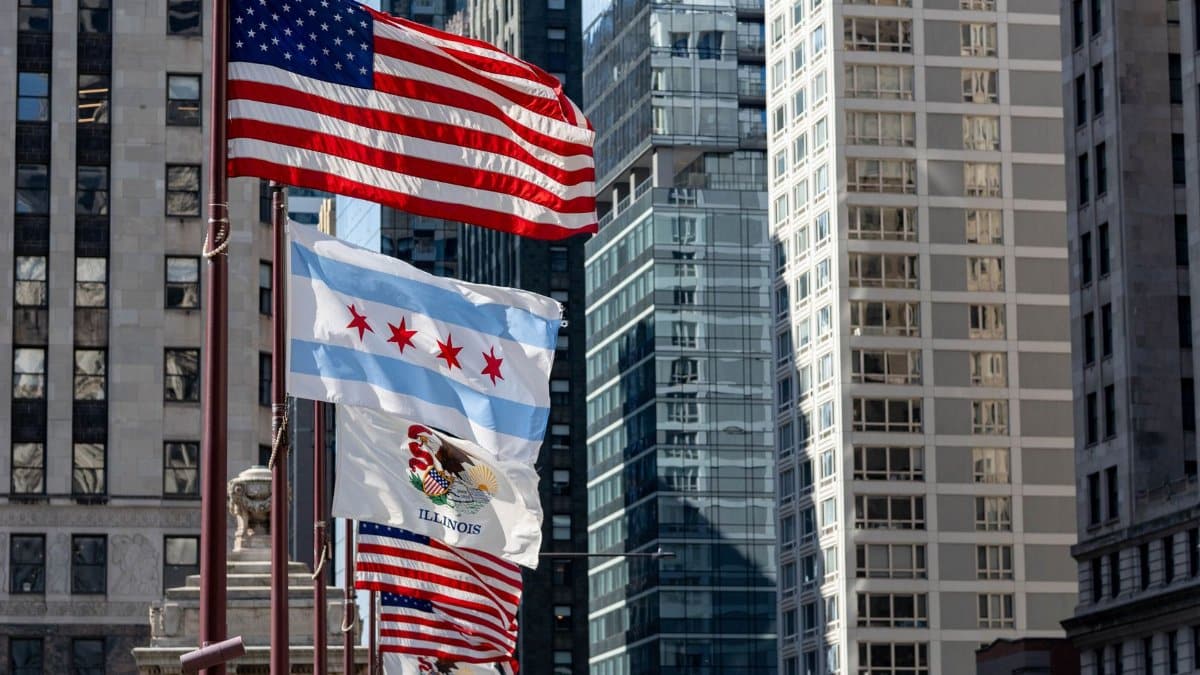Flags of the United States and Chicago against a backdrop of downtown skyscrapers.