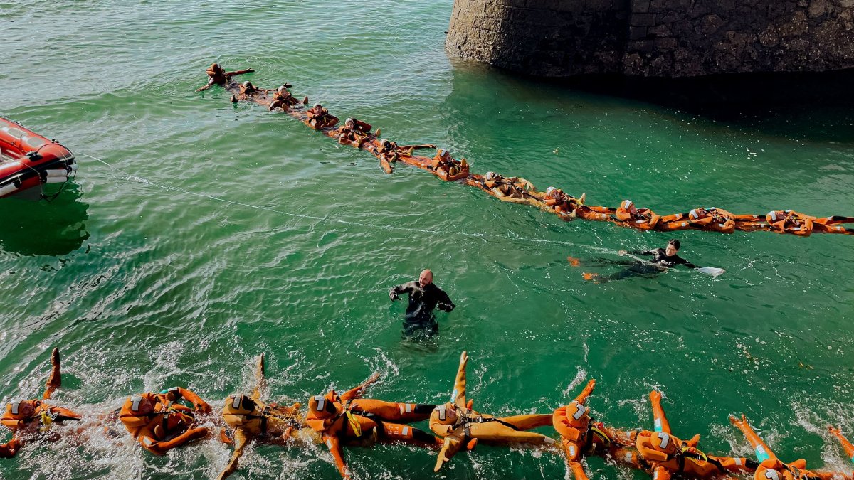People participating in a water rescue training exercise, linked by life vests.