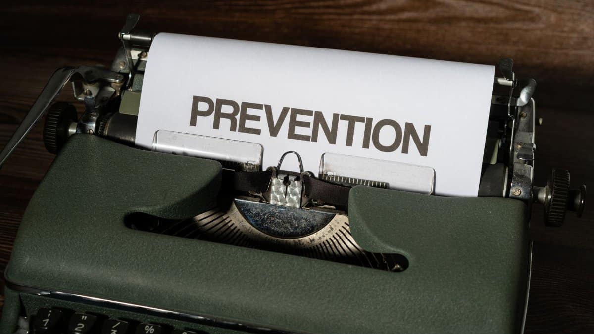 Close up of an antique typewriter with a white paper sheet displaying the word 'PREVENTION', placed on a wooden surface.