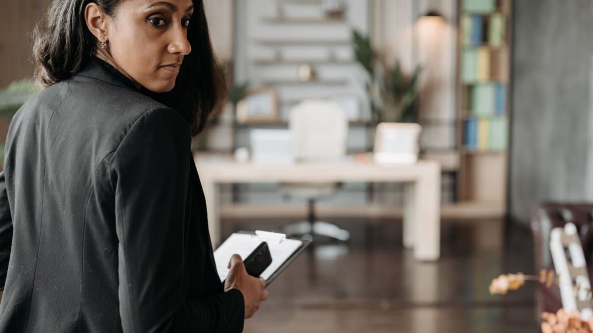 Confident businesswoman in a black suit holding a phone in a chic office interior.