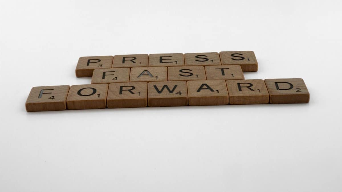 A motivational phrase 'Press Fast Forward' spelled with Scrabble pieces on a white background.