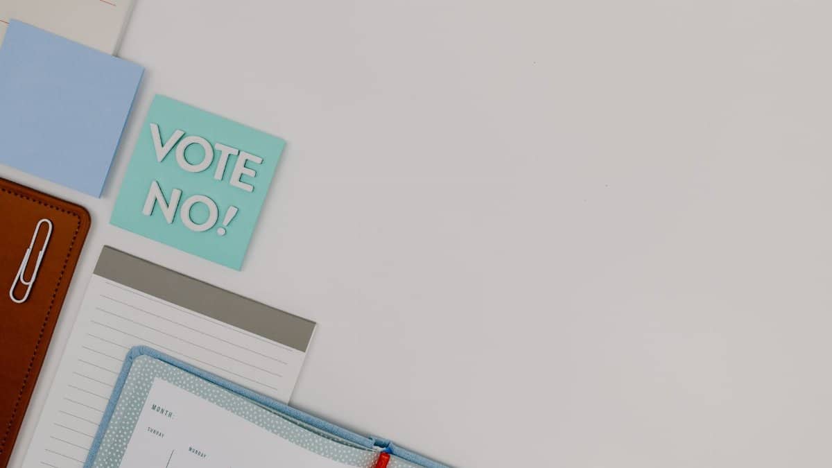 Flat lay of a workspace with a 'Vote No!' note, planner, and stationery items.