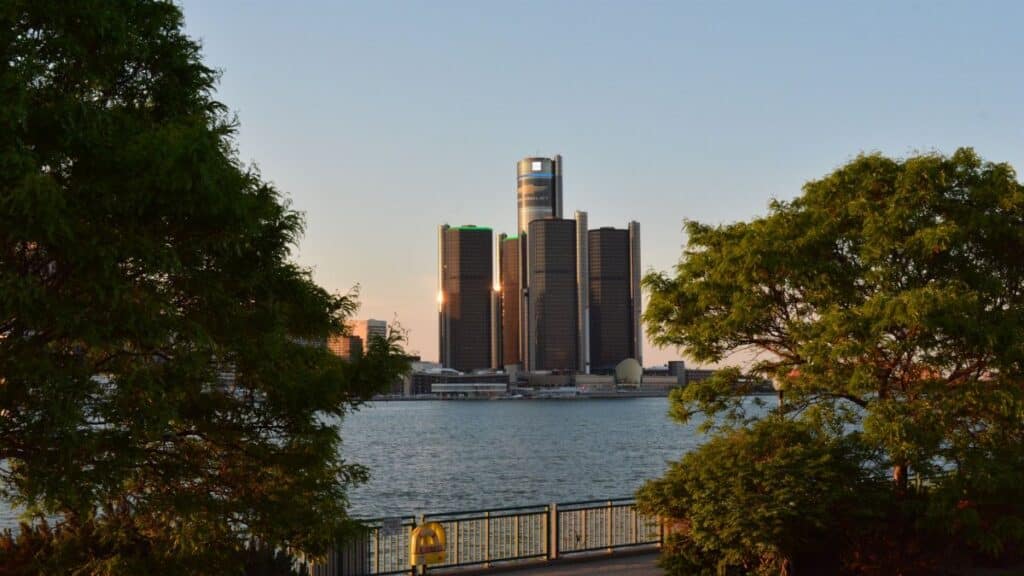 Scenic view of the Detroit Renaissance Center with lush trees framing the skyline at sunset.