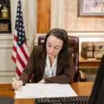 Female attorney in a law office signing legal documents at her desk, surrounded by legal books and symbols of justice.