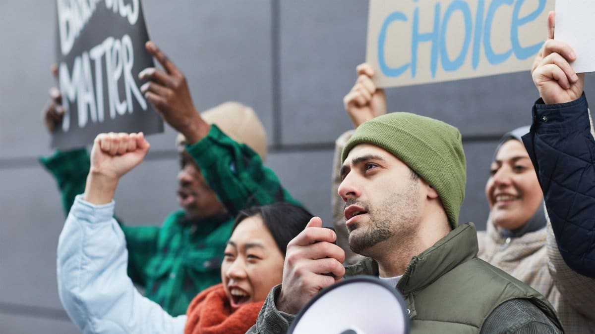 A diverse group of people passionately protesting with signs and a megaphone in an urban setting.