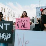 A diverse group of masked protesters holding signs that demand justice in an outdoor rally.