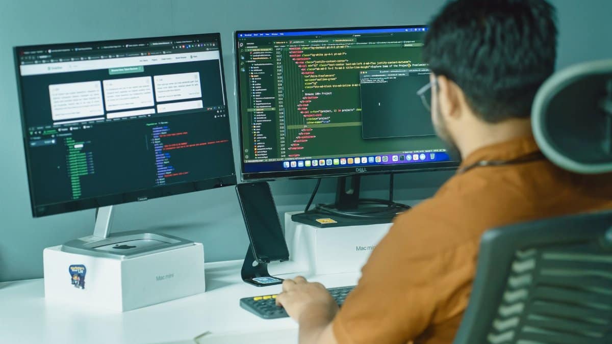 A software developer engaged in coding on dual monitors in a modern office setting.
