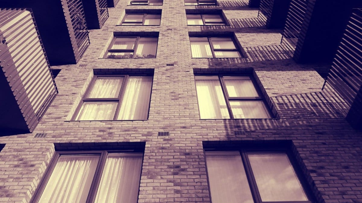Low angle view of a brick building with balconies and windows casting dramatic shadows.
