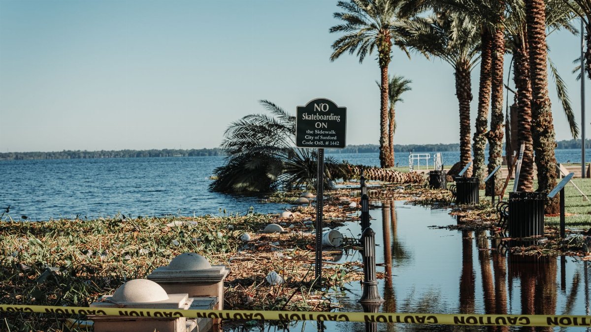 A flooded pathway with caution tape and palm trees by a lake in Sanford, Florida.