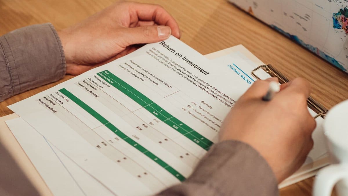A person analyzing a return on investment report with a pen in hand on a desk.