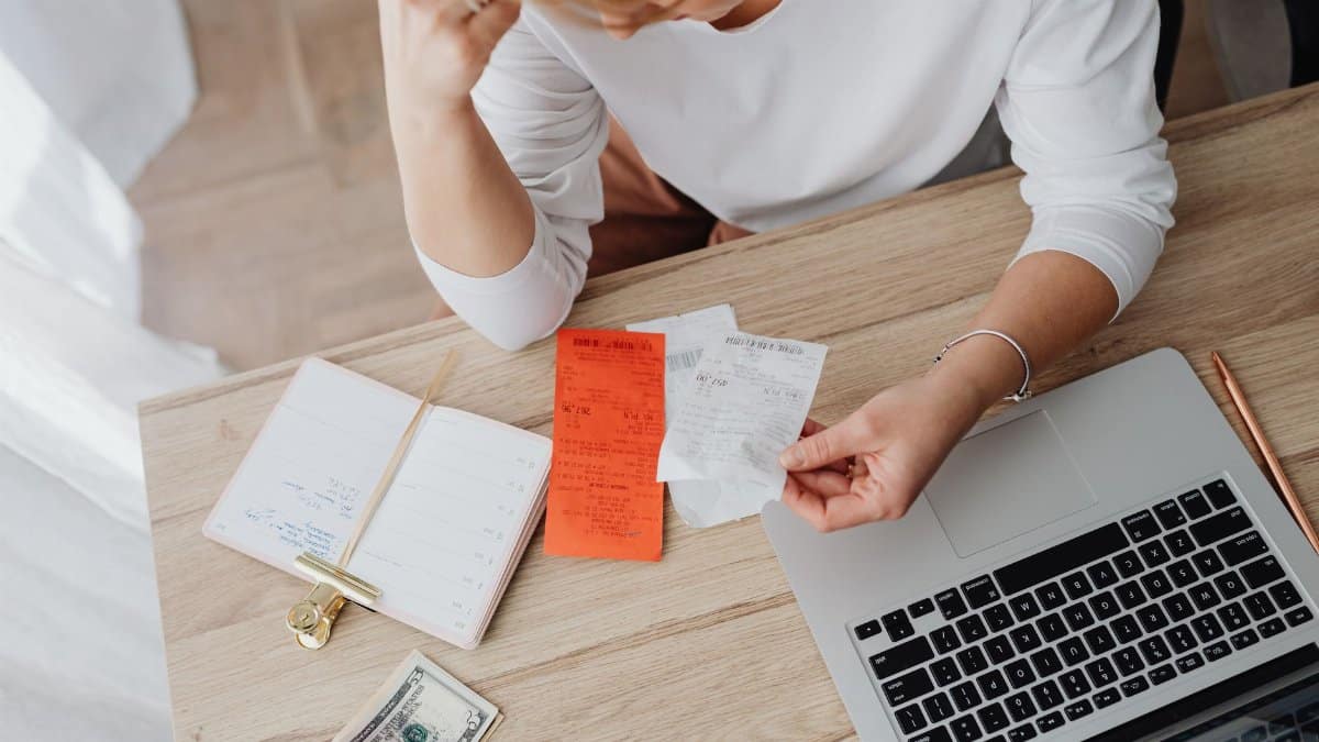 Woman reviewing receipts and planning budget using a laptop and notebook at home to manage expenses.