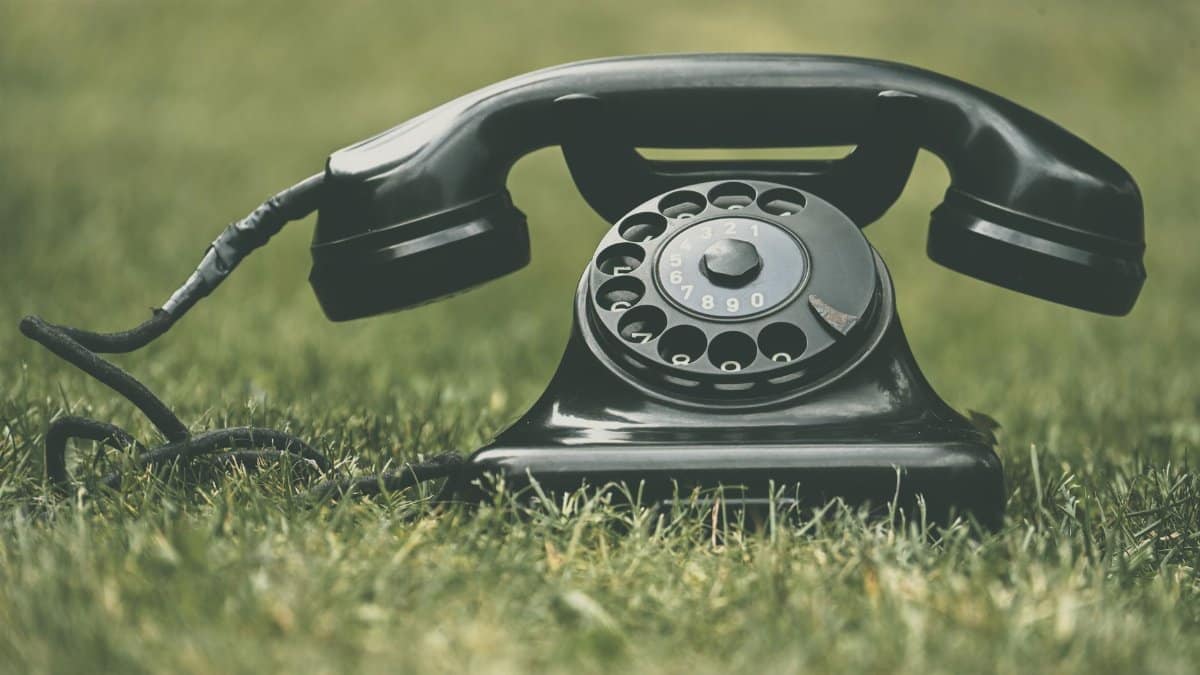 A classic black rotary dial telephone resting on green grass, highlighting vintage style.