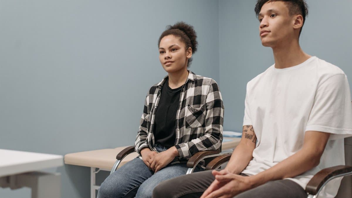 Two young adults sitting in a blue room, awaiting consultation in a minimalist setting.