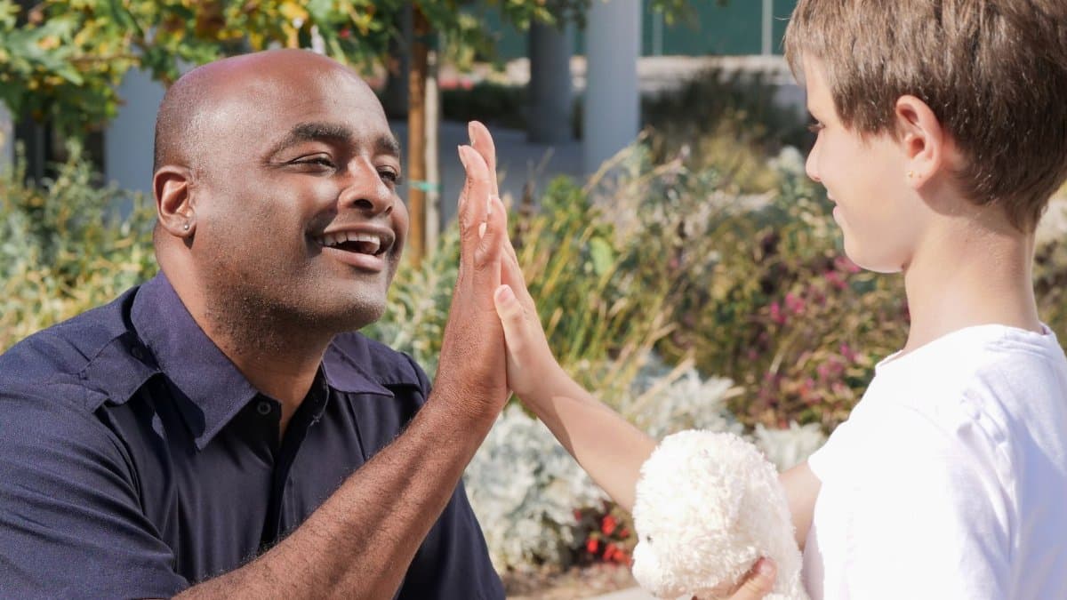 Police officer and child high-fiving outdoors, symbolizing community engagement.