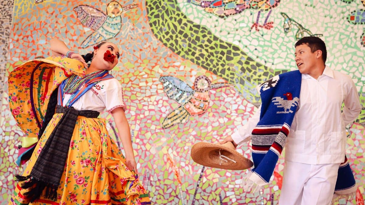 Colorful traditional Mexican dance in front of a mosaic mural depicting local wildlife.