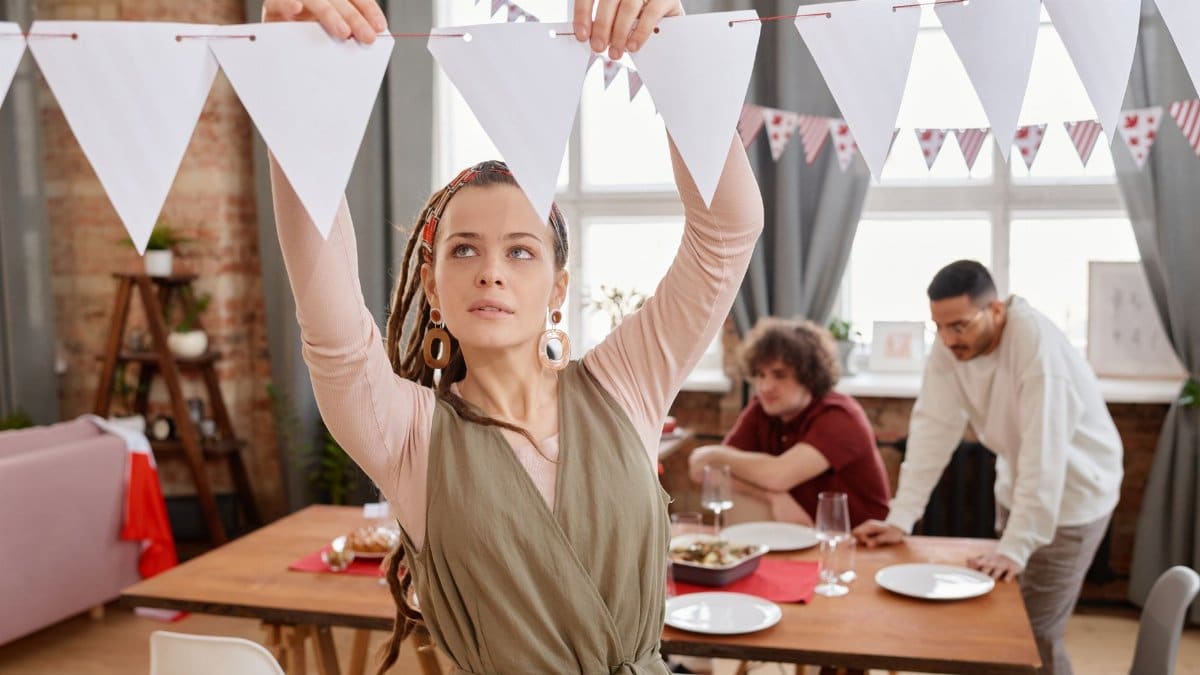 A woman decorates a dining room with bunting flags for a party gathering.