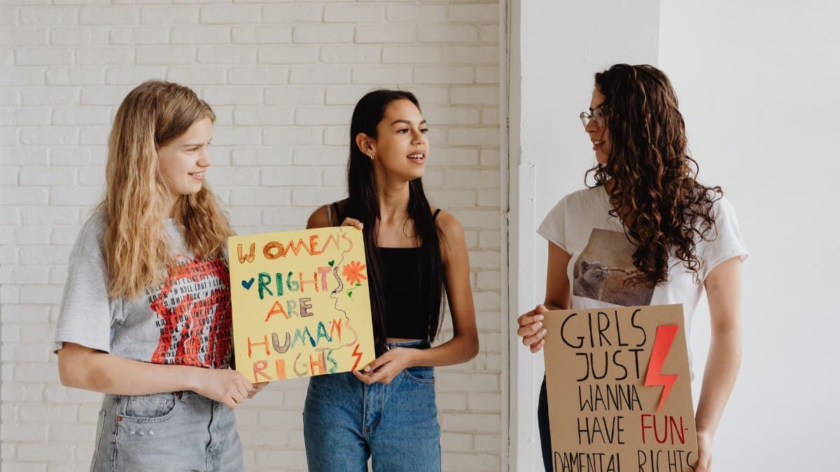 Three women holding advocacy signs supporting women's rights, indoors.