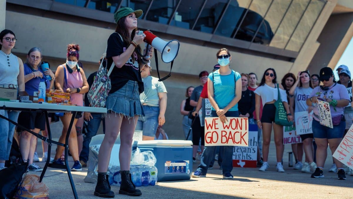 A diverse group of activists protest with signs and a megaphone at a women's rights rally.