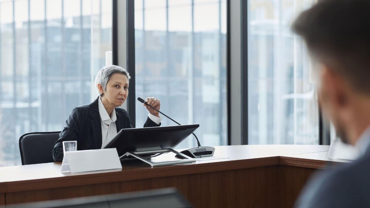 Businesswoman speaking at a corporate meeting in a modern office setting.