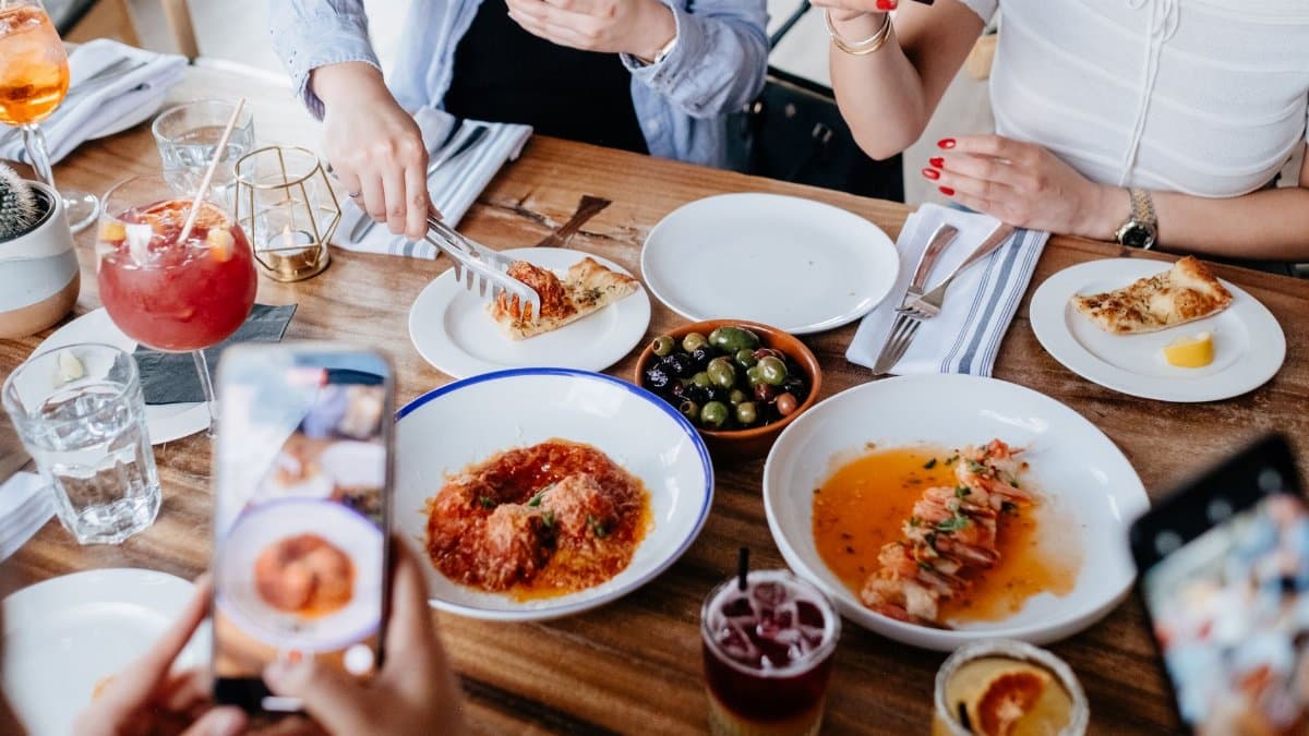 Women capturing their dining experience with smartphones in a restaurant setting.