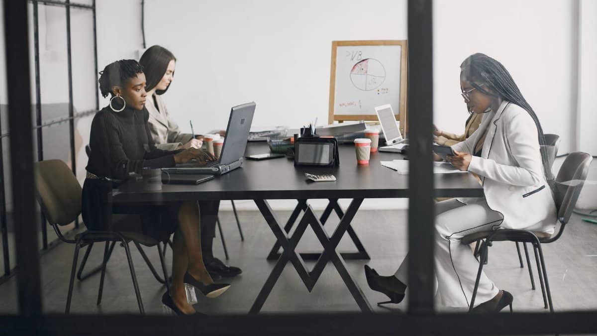 Three women engaged in teamwork and discussion around a table in a modern office setting.