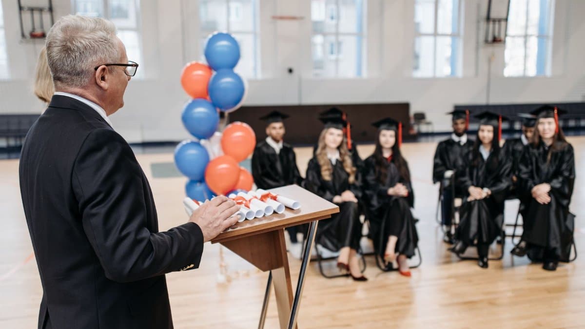 A formal graduation ceremony with a speaker addressing seated graduates in a gymnasium.