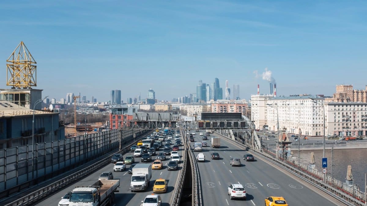 Highway traffic in Moscow with skyscrapers and river in the distance, showcasing urban life.
