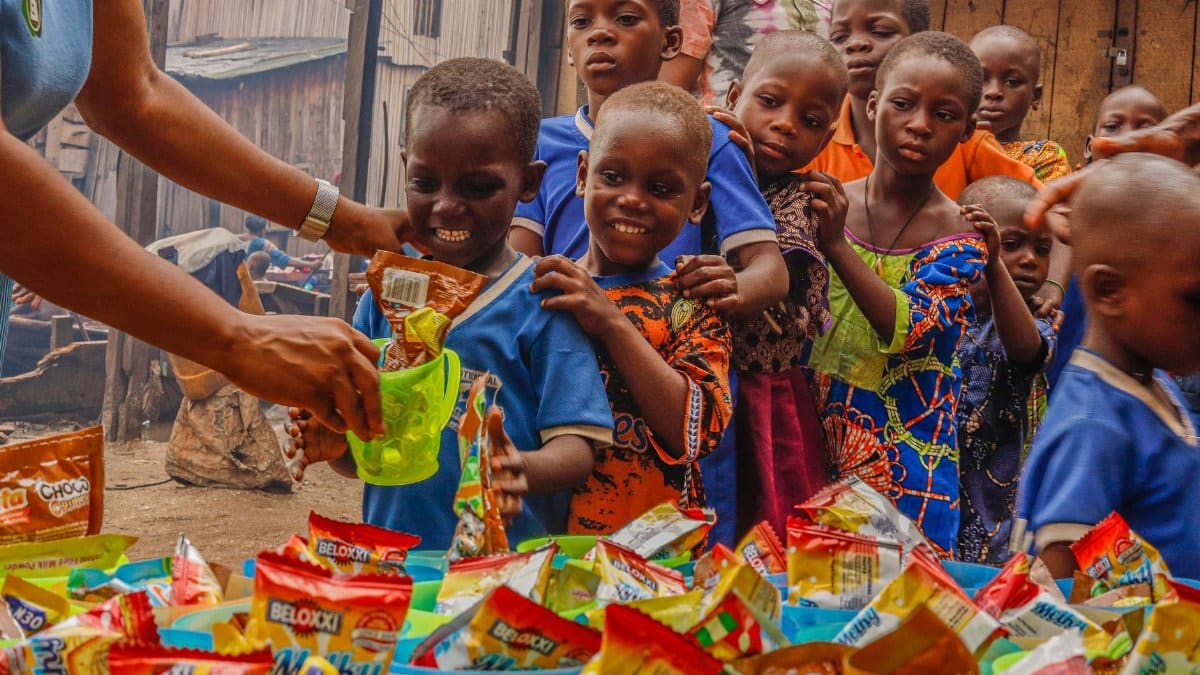 Joyful children receiving food supplies from a volunteer in an outdoor setting.
