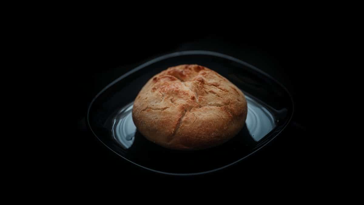 A fresh loaf of rustic artisan bread displayed on a black plate against a dark background.
