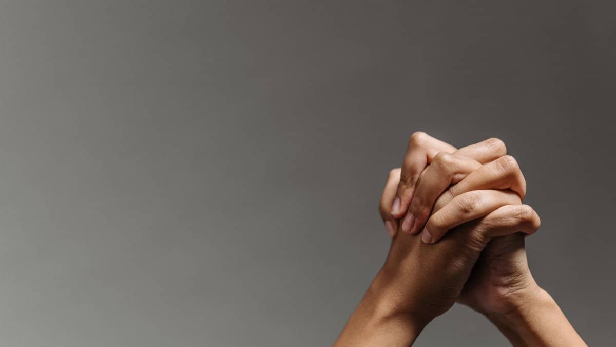 Close-up of two hands clasped together on a gray background, symbolizing unity and support.