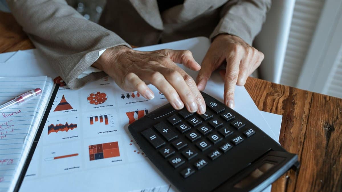 A businessman using a calculator to analyze financial charts and graphs on a desk.