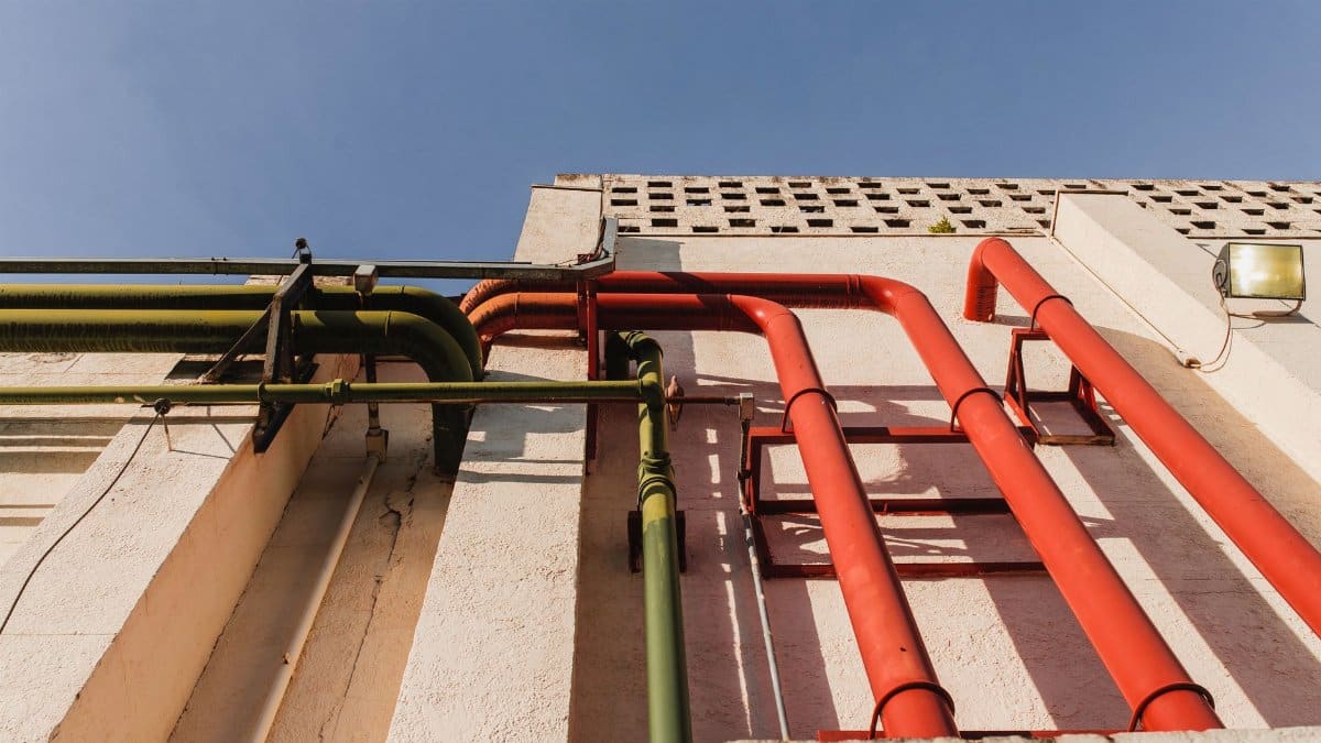 Close-up of vibrant red and green pipes on a sunlit urban building wall.